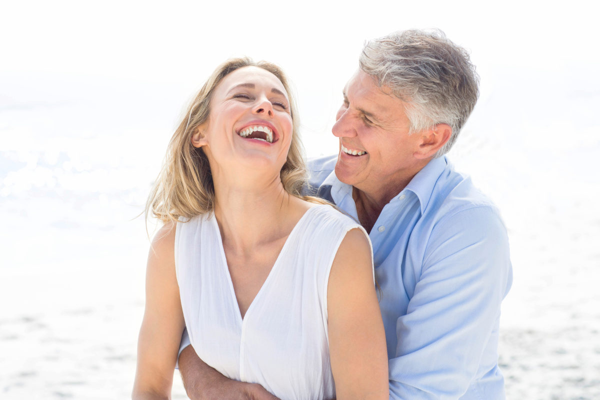 Happy couple laughing together at the beach | More Sex Can Prevent Heart Attacks, According To Science