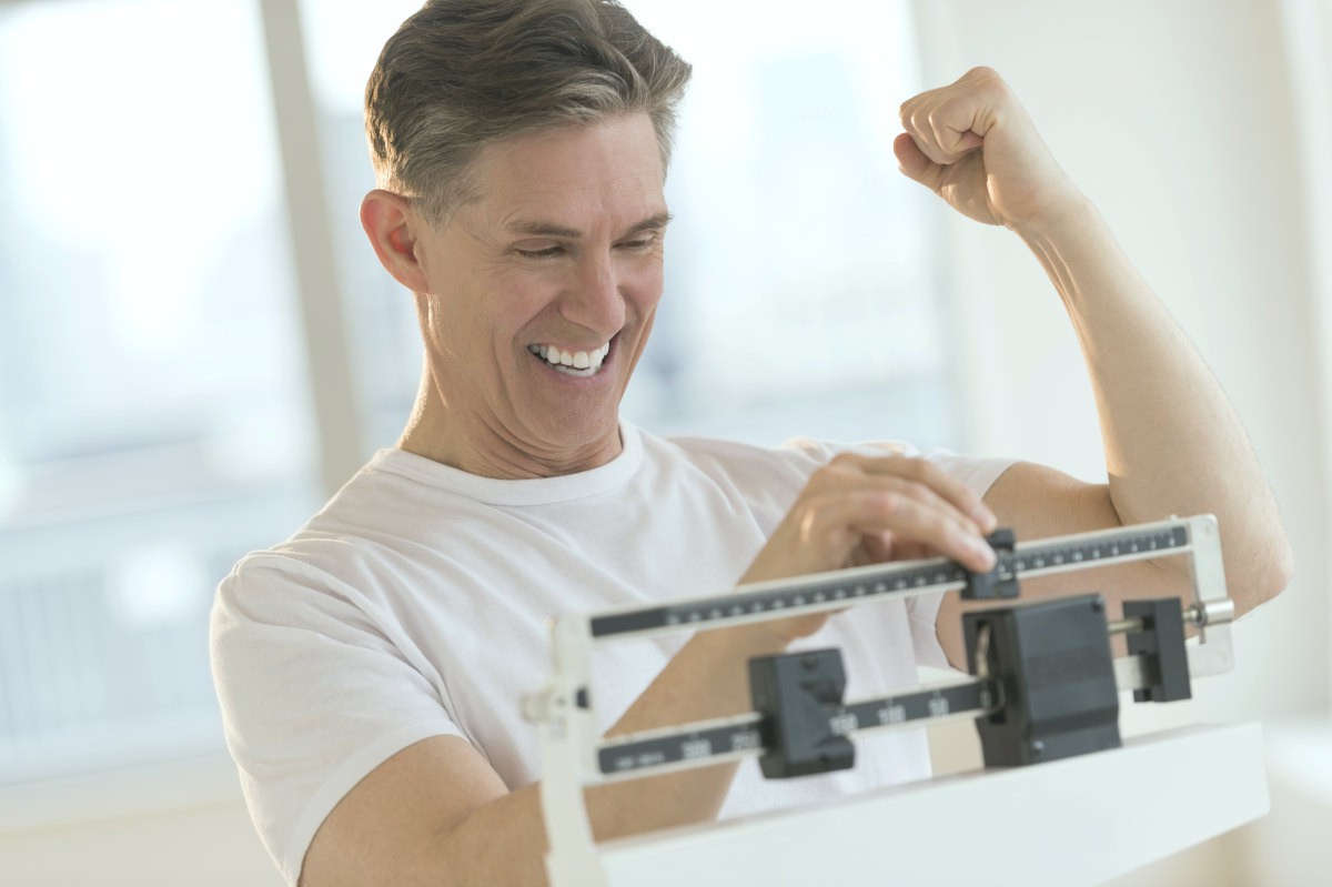 Excited mature man clenching fist while using balance weight scale at gym | How To Maintain Weight Loss In A Healthy Way | Maintaining