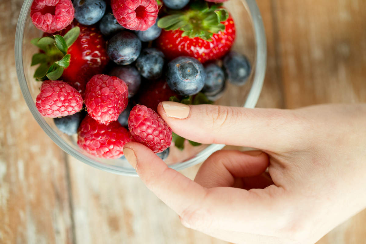 Woman hands with berries mix in glass bowl on wooden table | The Estrogen Family: Estrone, Estradiol, Estriol | estrogen function