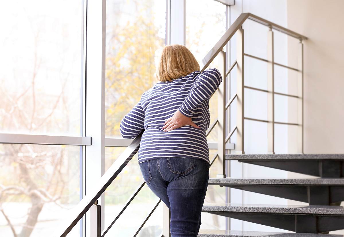 Senior woman suffering from backache while walking upstairs | HRT Hormone Replacement Therapy Frequently Asked Questions
