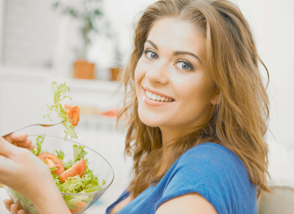 Young woman with long hair sitting on sofa at home and eating healthy food | How To Lower Estrogen Naturally | how to lower estrogen level