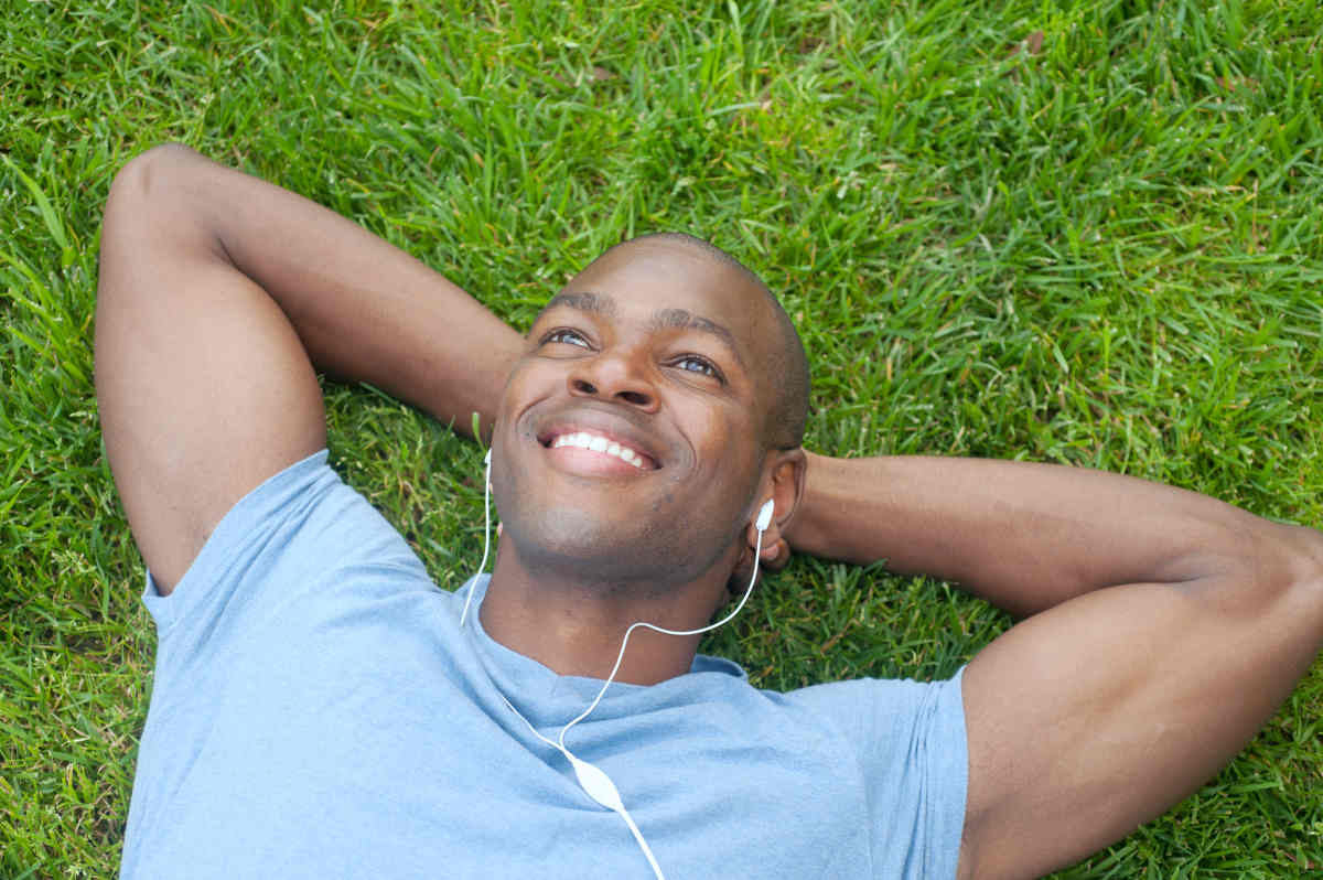 African American man lying in grass listening to music | The Ultimate List Of Brain Boosters: Ways To Increase Your Brain Power | boost your brain