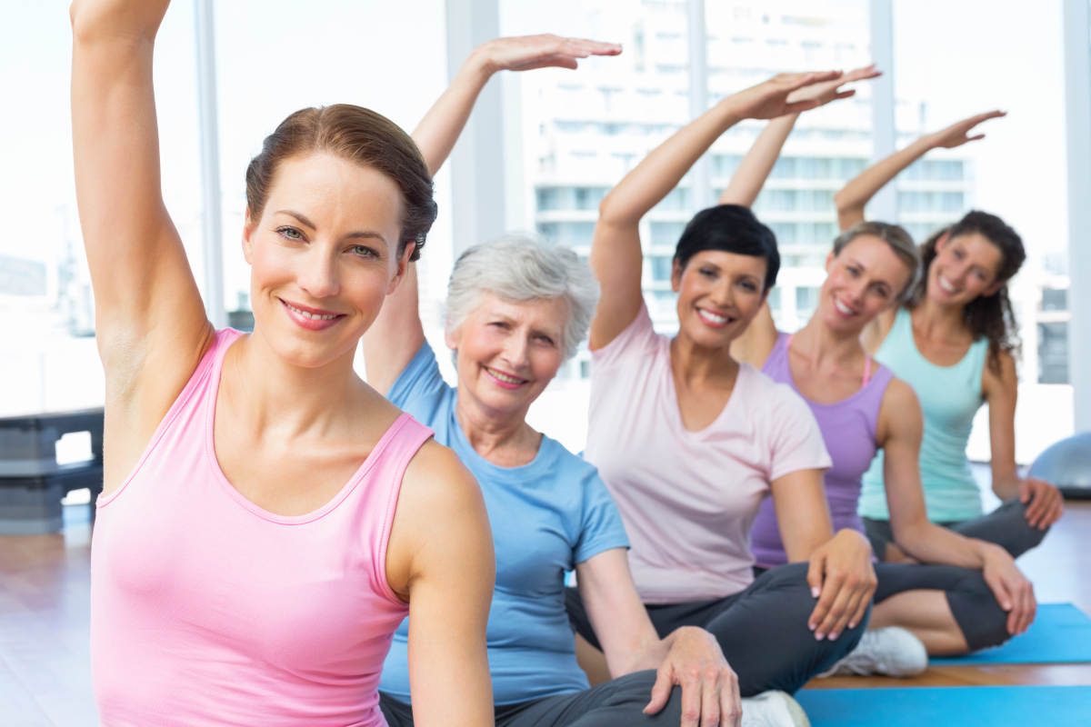 Smiling trainer with women in row stretching hands at yoga class | All About Menopause: Signs, Stages, Age, and Treatment | menopause treatment