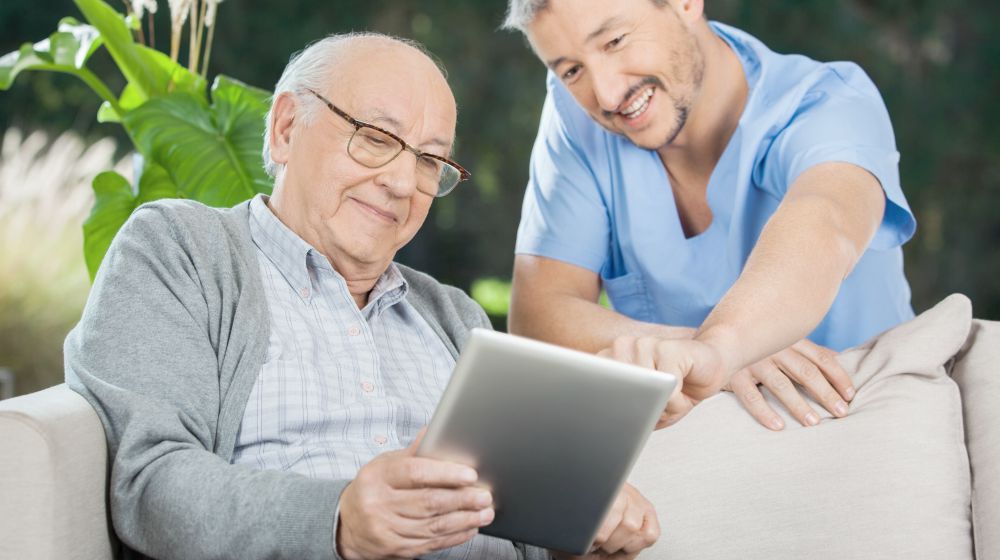 happy nurse helping senior man on his tablet | What Is Telehealth And How Does It Improve Your Healthcare? | what is telehealth | telehealth nursing