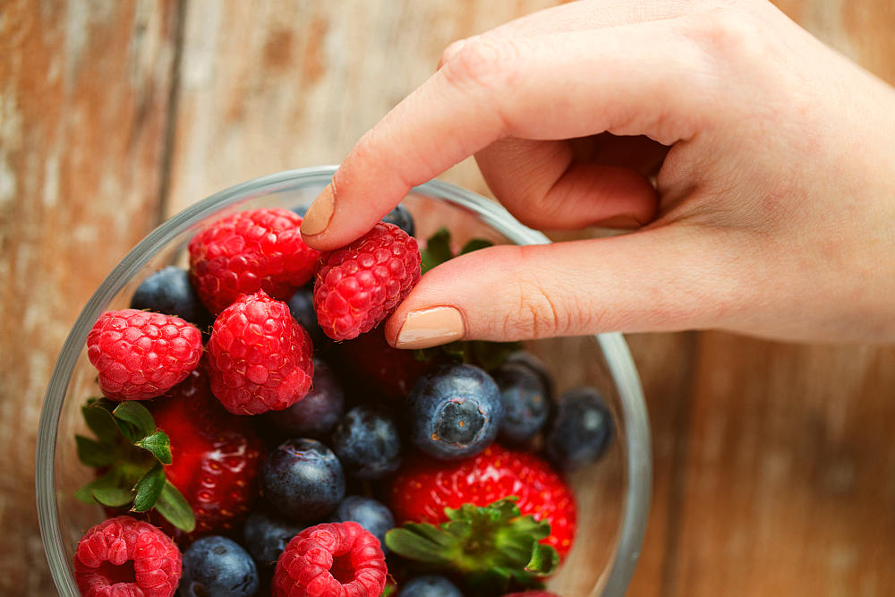 Woman hands with berries mix in glass bowl on wooden table | Best Fruits For Hypothyroidism | Hypothyroid Diet Food | thyroid healing foods