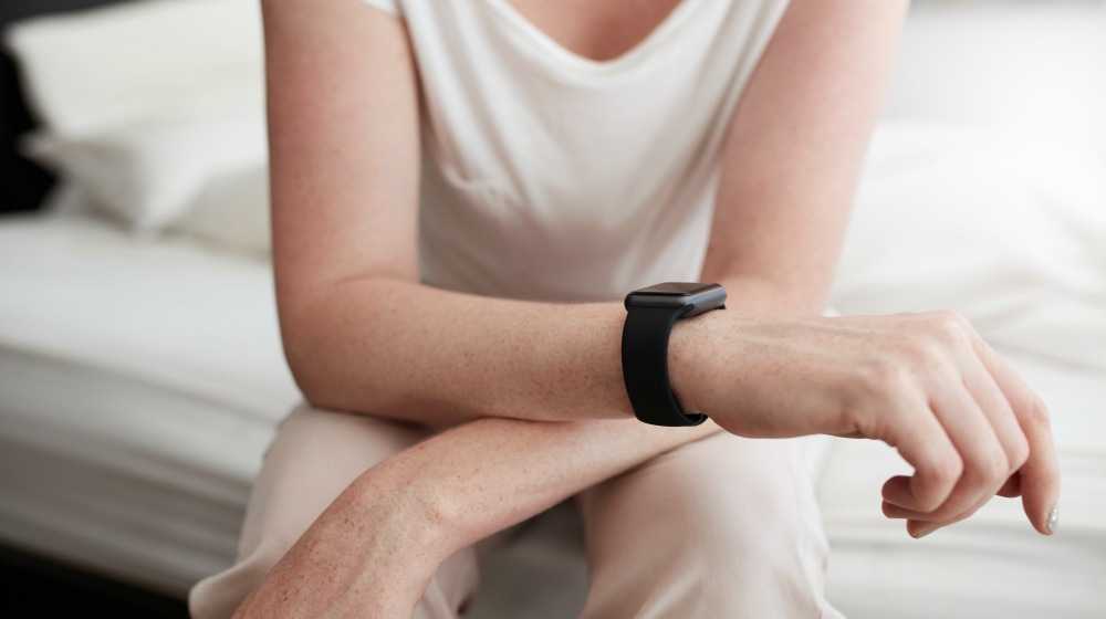 cropped shot of a woman sitting on bed wearing a wrist watch | The Impact of Lack of Sleep on Senescence | Aging and Sleep | aging and sleep | can lack of sleep make you sick