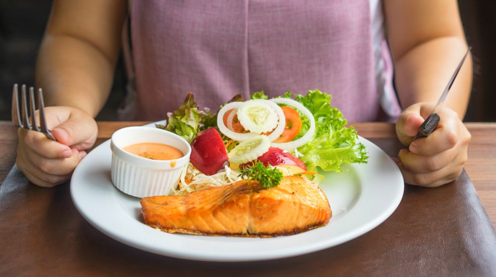person eating salmon steak | Hyperthyroidism Diet: Foods To Ease Symptoms | hyperthyroidism diet | hyperthyroidism natural treatment diet