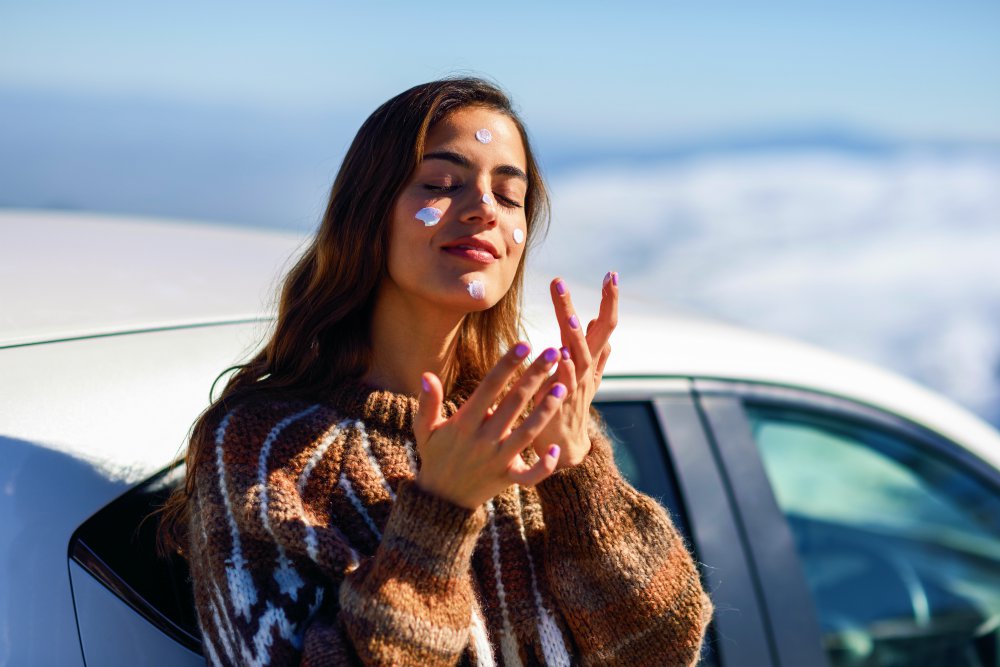 Young woman applying sunscreen on her face in snowy mountains in winter | Winter Skin Care Tips For Harsh, Cold, and Dry Weather | winter skin care | tip for dry skin
