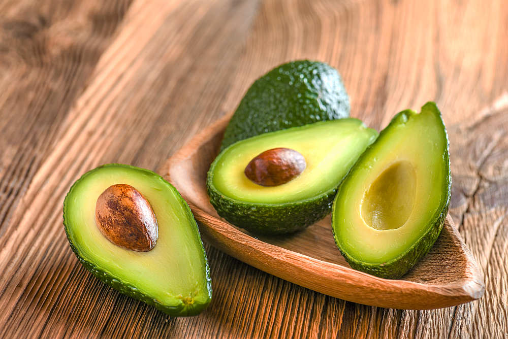 Avocado on old wooden table.Halfs on wooden bowl | Best Testosterone Boosters To Add To Your Diet | testosterone boosting foods
