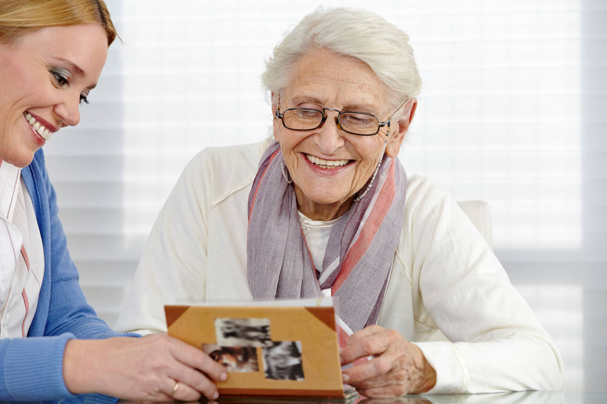 Happy senior woman watching photo album with eldercare nurse | Memory Lapses: What's Normal And When To Seek Help | difference between alzheimer's and dementia | memory lapse