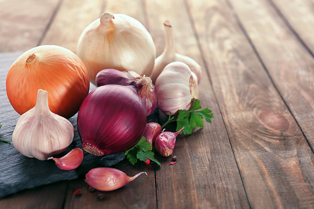 Slate plate with fresh garlic and onion on wooden table | Best Testosterone Boosters To Add To Your Diet | testosterone boosting foods list