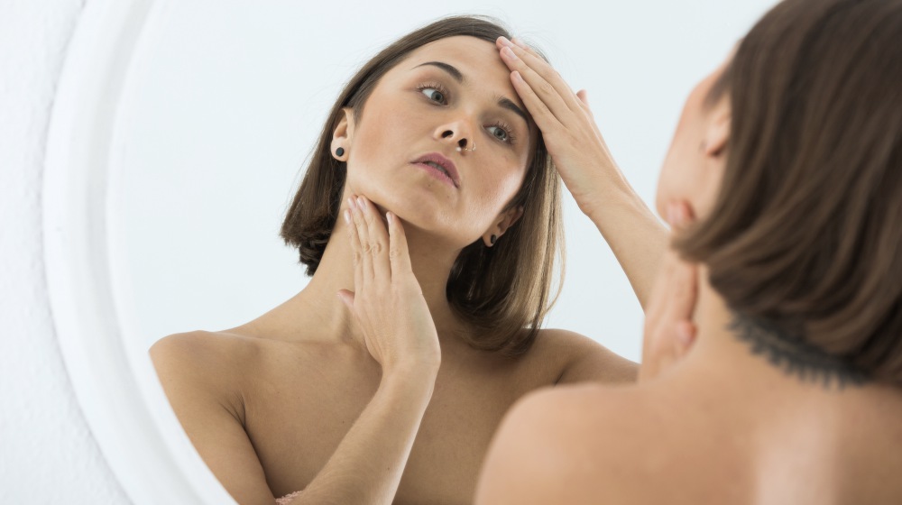 young woman checking her face in mirror | Thyroid Neck Check: A Step-By-Step Guide For Thyroid Disorders | thyroid neck check | thyroid test